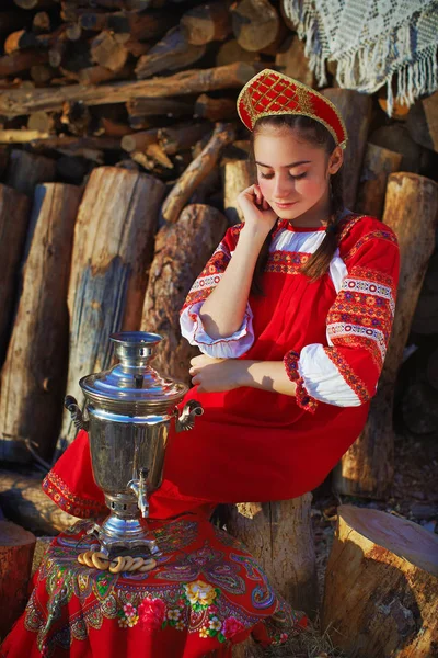 Красивая девушка в русский народный костюм сидит возле Самовар и улыбается — стоковое фото