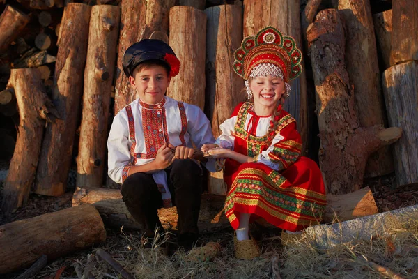 Два российских детей в русские народные костюмы, мальчик и девочка, играя вместе и эмоционально улыбается — стоковое фото
